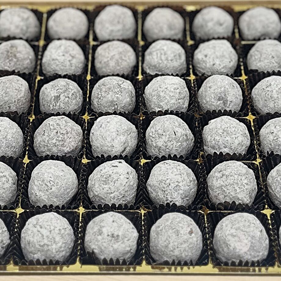 36 Champagnertrüffel in einer hochwertigen Holzbox, einzeln in dunklen Papierförmchen angeordnet, auf goldenem Tablett präsentiert. Perfektes Geschenk für Genießer edler Pralinen zu festlichen Anlässen.