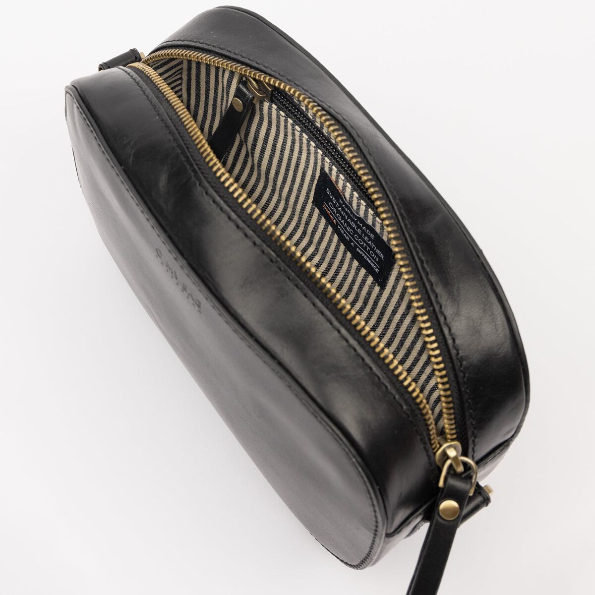 Schwarze Umhängetasche aus Leder in kompakter Größe, mit goldfarbenem Reißverschluss geöffnet und einem gestreiften Innenfutter in Beige und Dunkelgrau, auf hellem Hintergrund fotografiert.