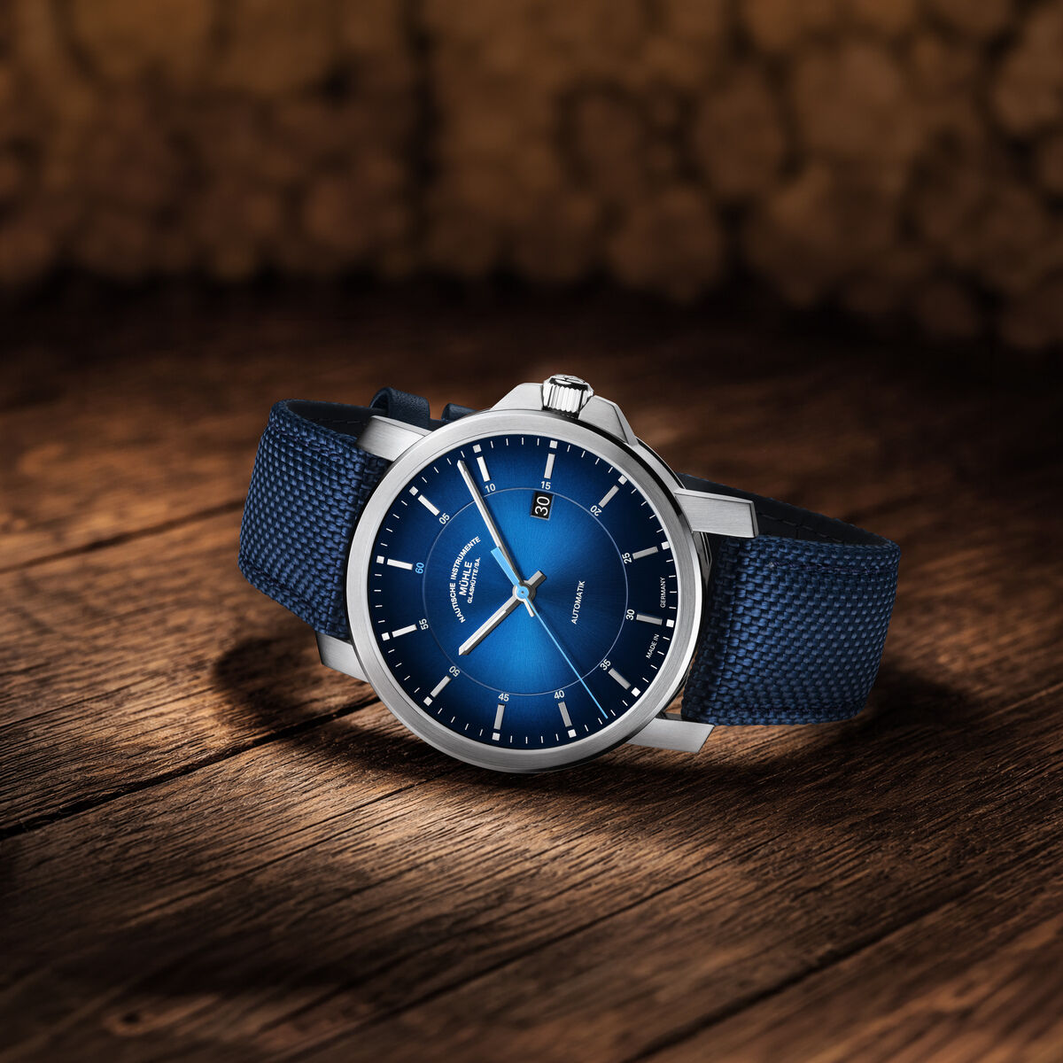 Die Automatikuhr »29er« Casual ZEIT-Sonderedition (2026) von Mühle-Glashütte liegt auf einem Holzuntergrund. Das Gehäuse aus Edelstahl, das blaue Zifferblatt und das dunkelblaue Canvas-Lederarmband stehen im Kontrast zum warmen Holzhintergrund. Die Uhr wirkt elegant und modern.