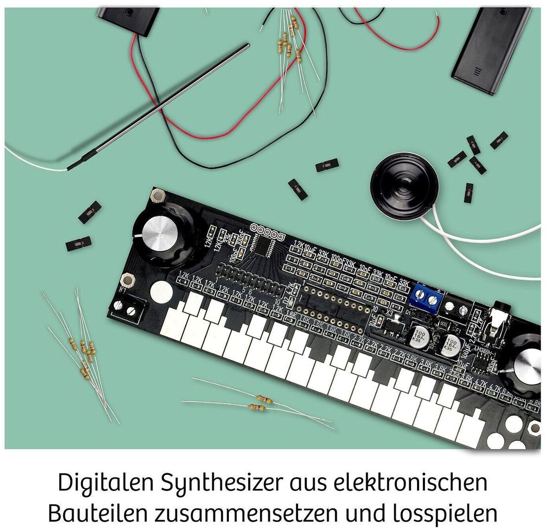 Ein digitaler Synthesizer-Bausatz mit zahlreichen elektronischen Bauteilen, die auf einer grünen Oberfläche verteilt sind. Der Synthesizer selbst hat eine schwarze Basis mit weißen Tasten und diversen Anschlüssen und Schaltkreisen.