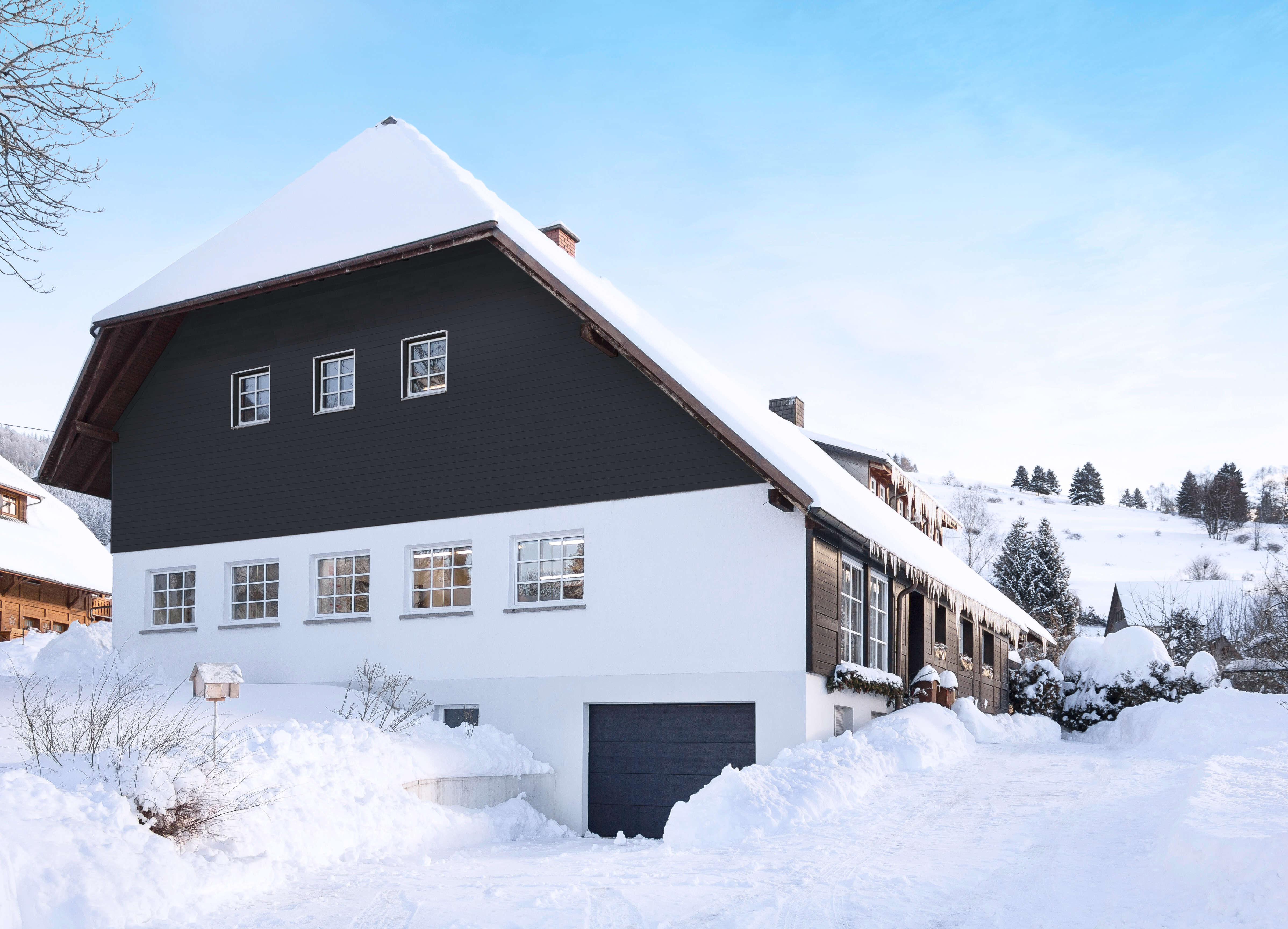 Zweistöckiges Haus mit schwarzer und weißer Fassade, schneebedecktem Dach und verschneiter Umgebung im Winter