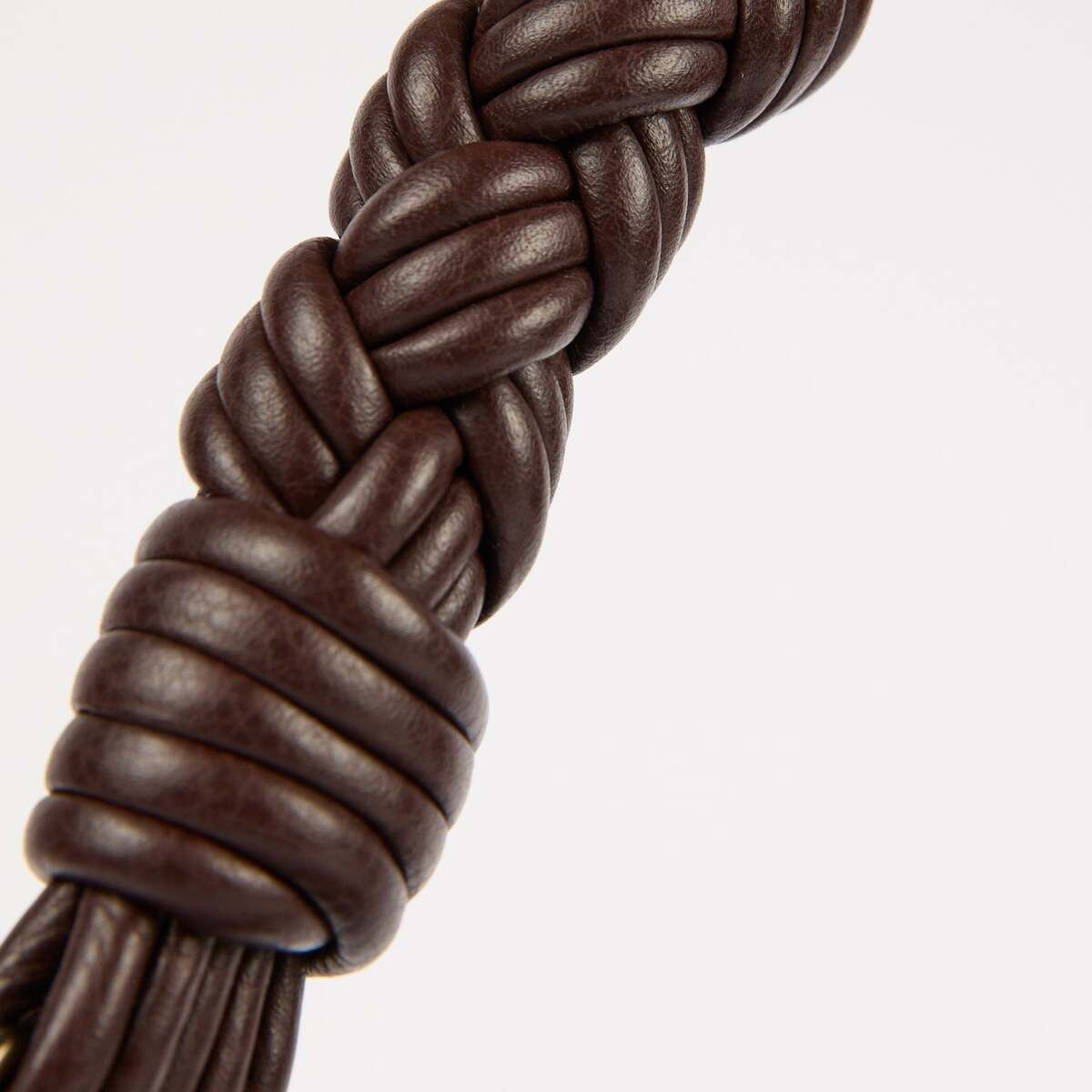 Nahaufnahme eines geflochtenen dunkelbraunen Henkels einer Tasche »Leo« in Lederoptik, aufgenommen vor hellem, neutralem Hintergrund. Das strukturierte Flechtmuster steht im Mittelpunkt und betont die hochwertige, modische Verarbeitung des Accessoires.