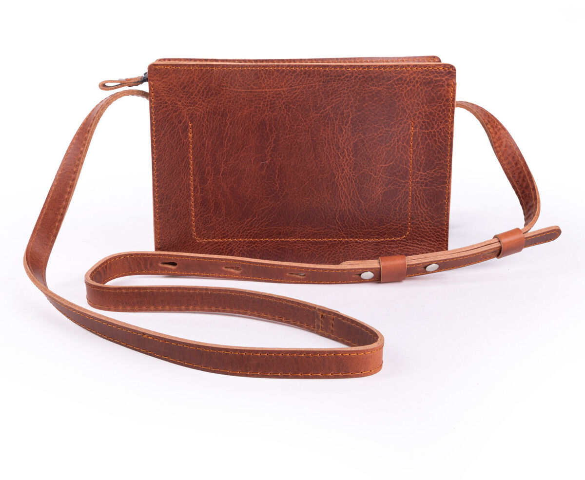 Kernledertasche 'Sas' aus braunem, leicht glänzenden Leder mit abnehmbarer, verstellbarer Schulterriemen. Die Tasche steht aufrecht vor weißem Hintergrund und ist minimalistisch sowie traditionell verarbeitet. Geeignet für Alltag, Jagd oder Freizeit.