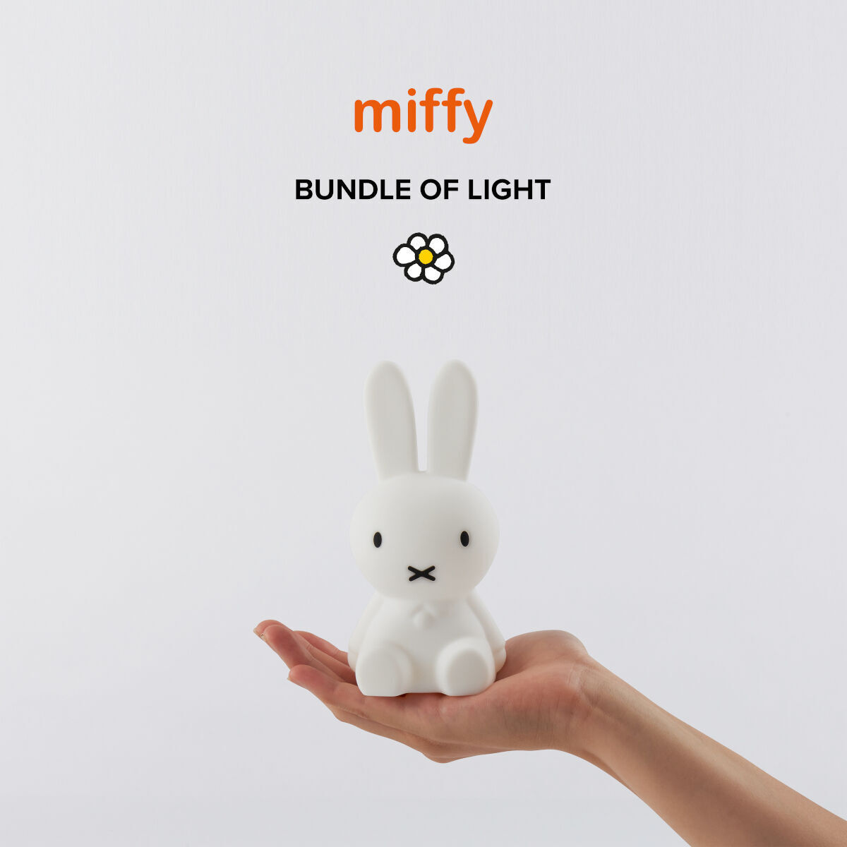 Ein kleines Nachtlicht in Form der Hasenfigur Miffy, das in einer Hand gehalten wird. Das Licht ist überwiegend weiß mit einigen schwarzen Details. Oben im Bild steht 'miffy' in orangefarbener Schrift mit dem Zusatz 'BUNDLE OF LIGHT'.