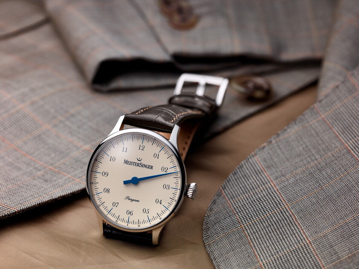 Die ZEIT-Sonderedition »Pangaea« von MeisterSinger kombiniert ein zeitloses, minimalistisches Design mit einem grauen Lederarmband und einem Edelstahlgehäuse. Die Uhr liegt auf einem grauen Anzug mit feinen Karos, die Knöpfe sind sichtbar.