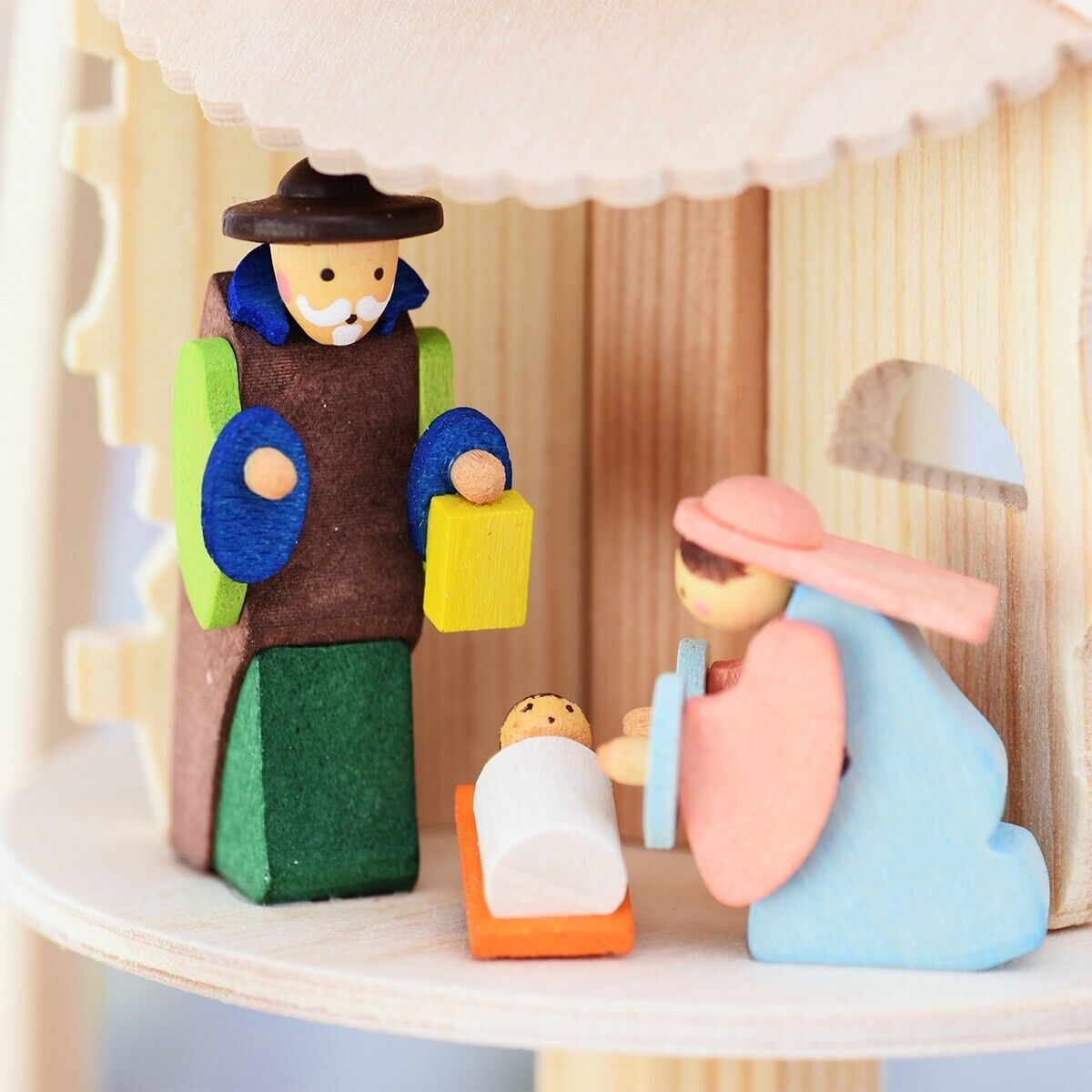 Holzdekoration in Pyramidenform mit Figuren der Geburt Christi. Ein Mann hält ein gelbes Geschenk, Maria kniet und hält ihre Hände über das Jesuskind in der Krippe.