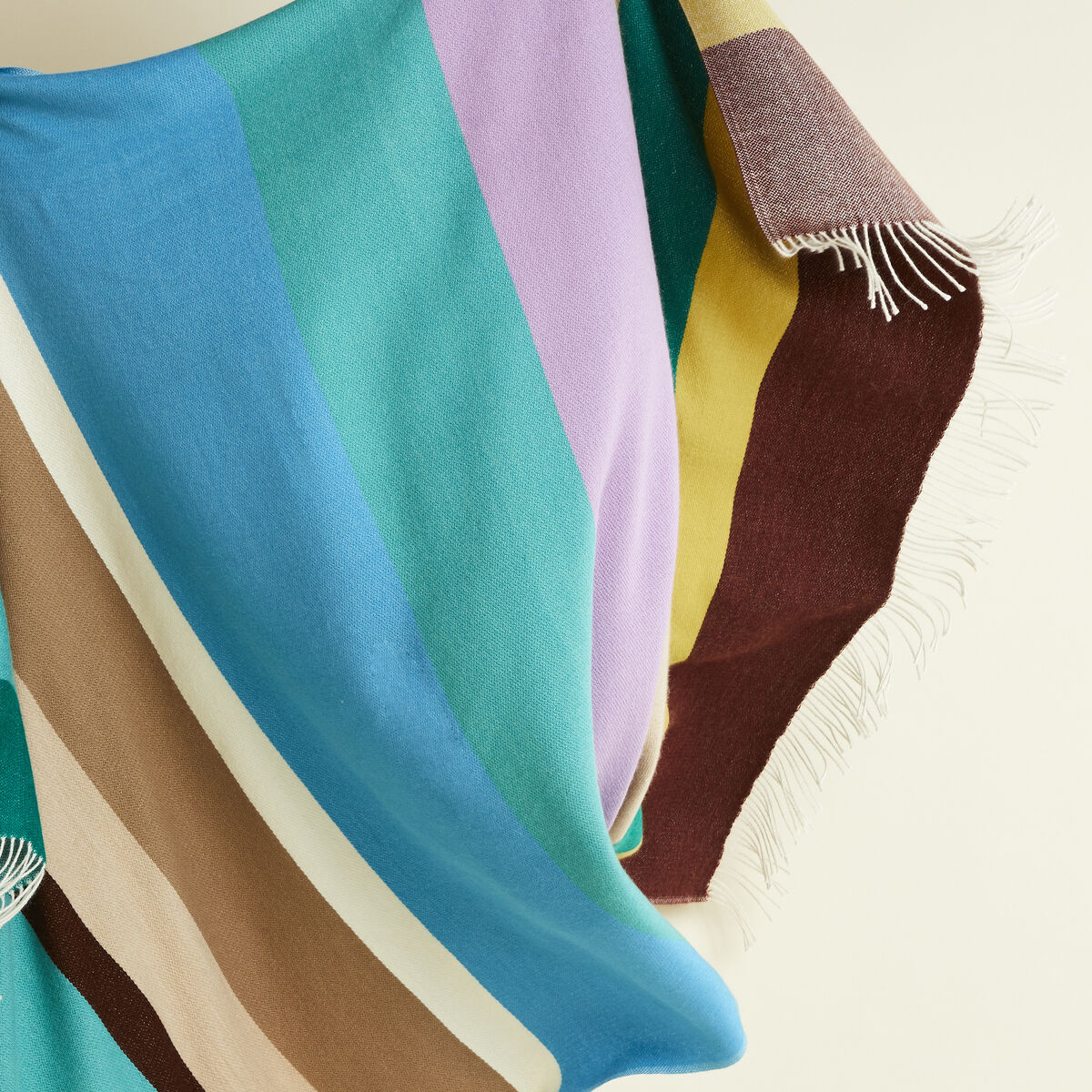 Eleganter Cape »Mainau« aus 100% Alpaka der Marke parati. Der Stoff zeigt eine feine, weiche Struktur in sanftem Beige und Creme mit breiten, fließenden Linien. Der Umhang wirkt voluminös und edel, fällt sanft, und ist ideal als stilvolles Accessoire für den Winter.