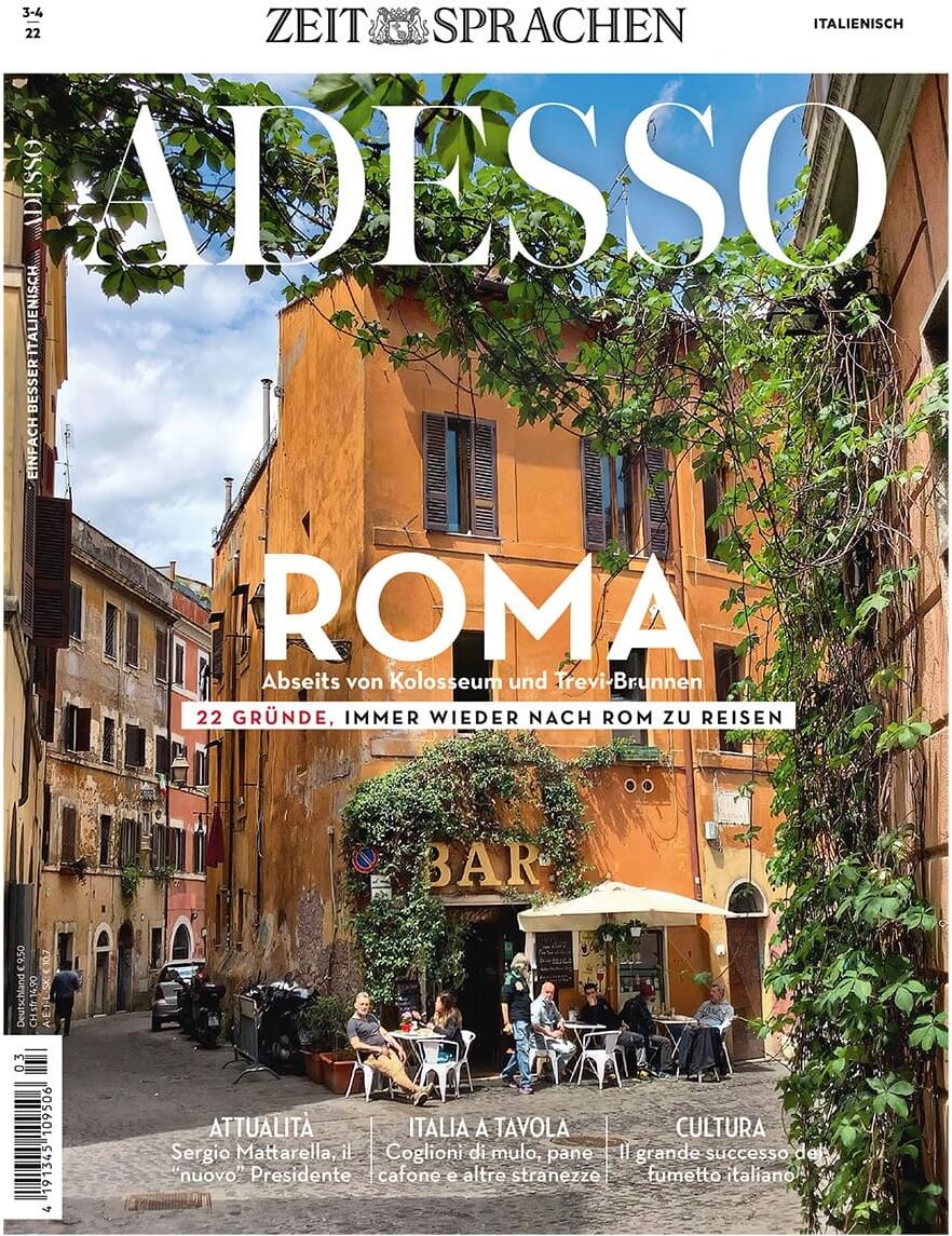 Titelblatt der Zeitschrift 'Adesso' vom März 2022. Im Fokus steht eine malerische Straßenszene in Rom mit einem gemütlichen Café, umgeben von bunten Gebäuden und Grünpflanzen.