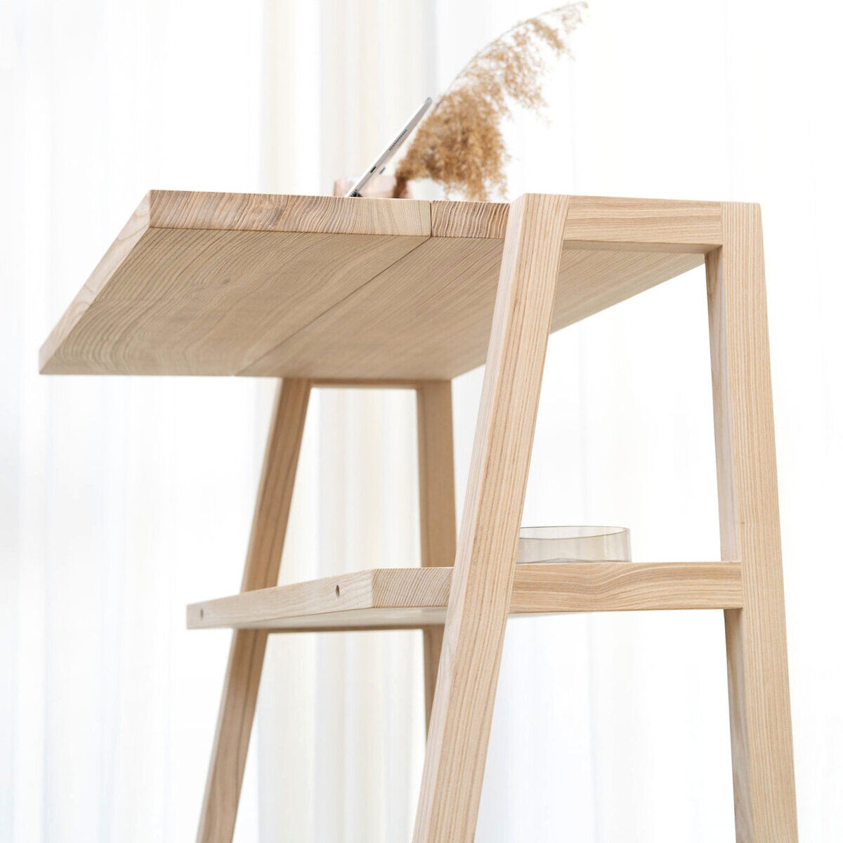 Das Bild zeigt das KultPult "SCALA" von Frau Caze, ein modernes Stehpult aus hellem Holz mit klaren Linien. Auf der oberen Ablage steht ein Glas mit Trockenblumen. Der Hintergrund ist hell und lichtdurchflutet, die Gestaltung wirkt minimalistisch und elegant.