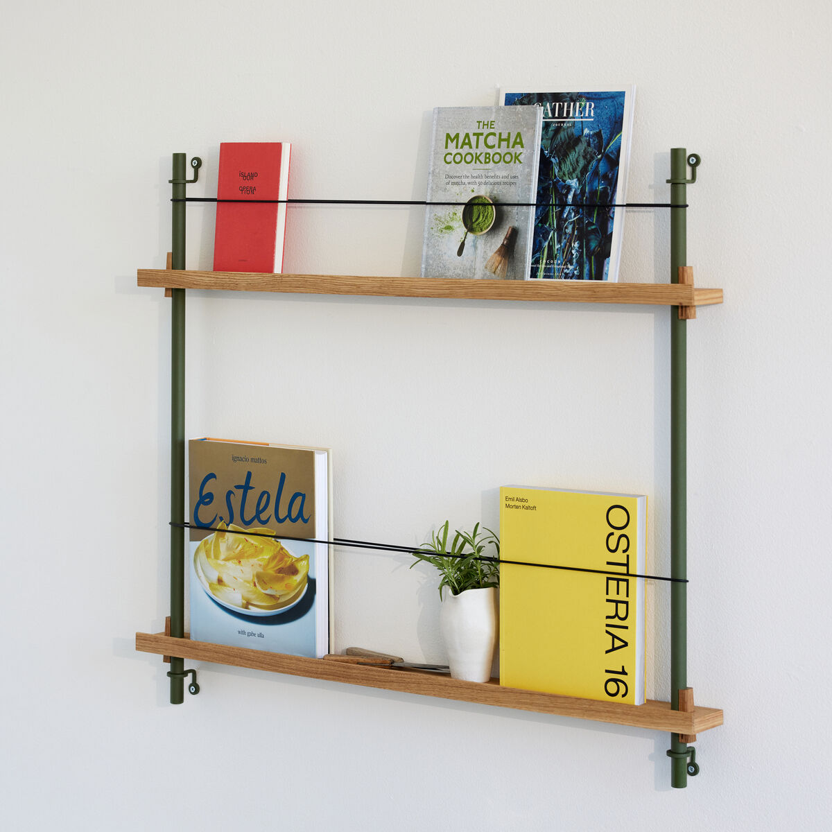 Ein modernes Wandregal aus Holz und Metall mit zwei Regalböden. Auf den Regalböden stehen verschiedene Bücher, eine kleine Pflanze und dekorative Gegenstände. Darunter befindet sich ein Schreibtisch mit geöffnetem Buch, Glasbechern und Büro-Utensilien. Die Wand ist weiß gestrichen.