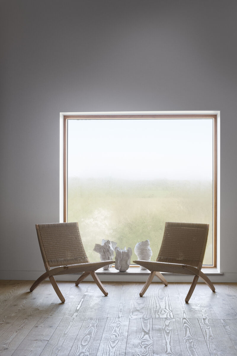Zwei geflochtene Cuba Chairs von MG501 aus Holz, die vor einem großen Panoramafenster stehen, durch das ein nebliger Ausblick auf eine grüne Landschaft zu sehen ist.
