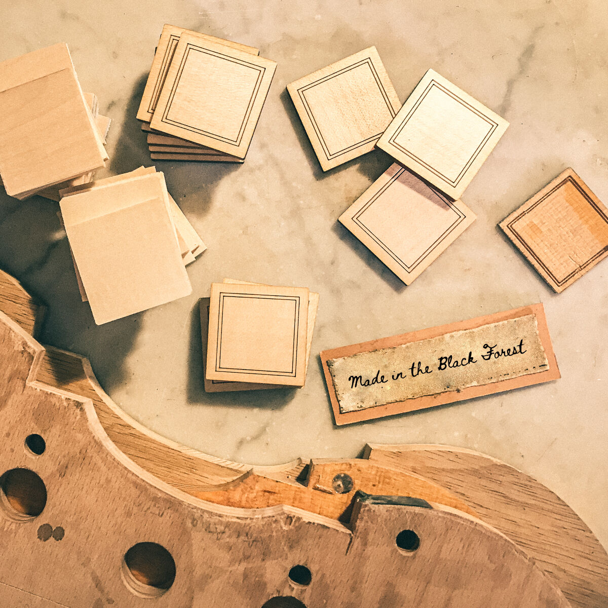 Eine Sammlung von Holzspielen mit quadratischen Holzstücken und einem Schild, das 'Made in the Black Forest' zeigt. Im Hintergrund sind unvollständige Teile eines Spielbretts zu sehen.