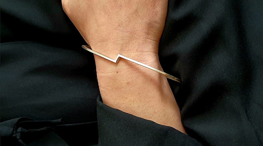 Schmale, silberne Armspange mit Zickzack-Design am Handgelenk einer Person mit schwarzer Kleidung