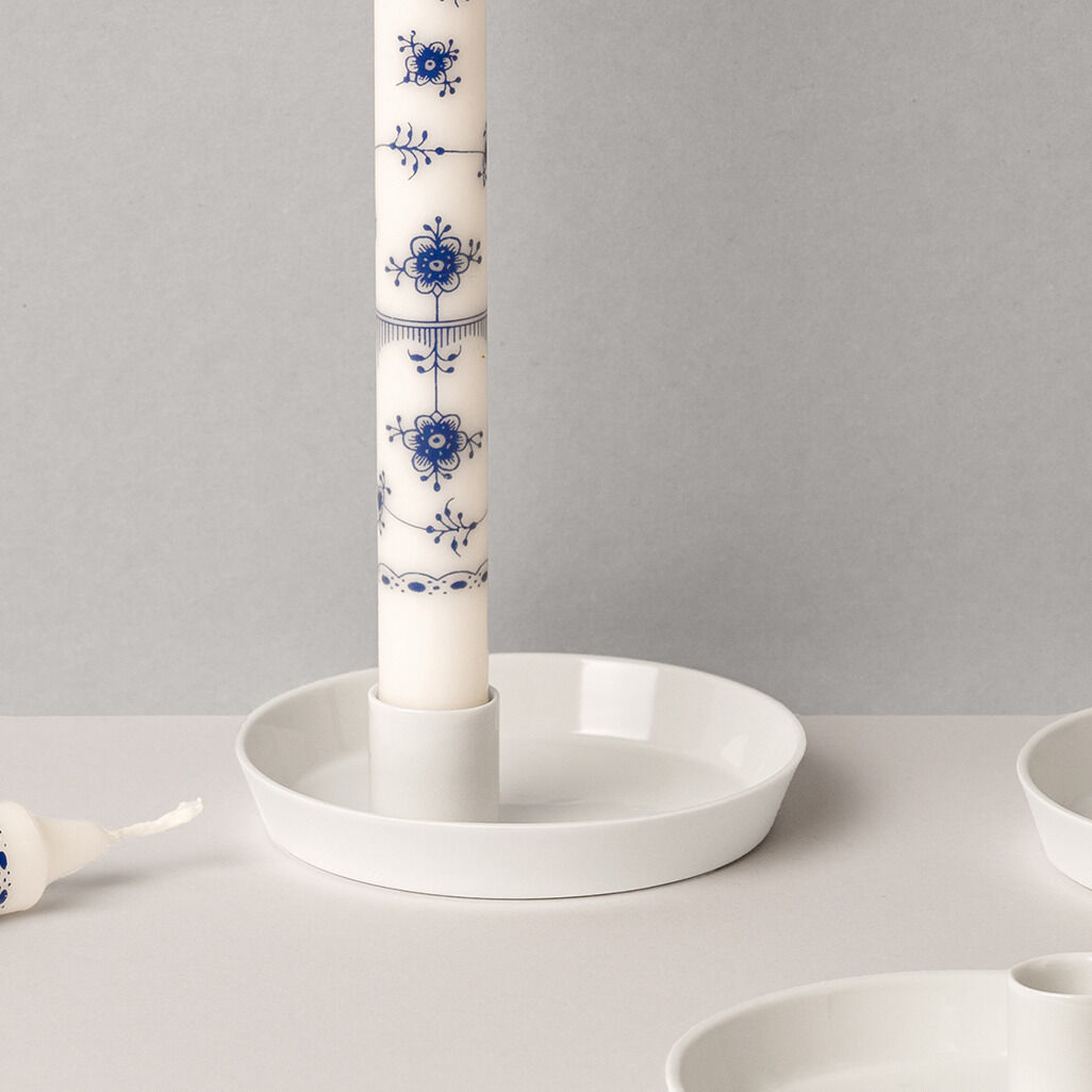 Kerzenhalter aus Porzellan mit blauem floralen Muster, darauf eine weiße Kerze, auf einem neutralen Hintergrund platziert.