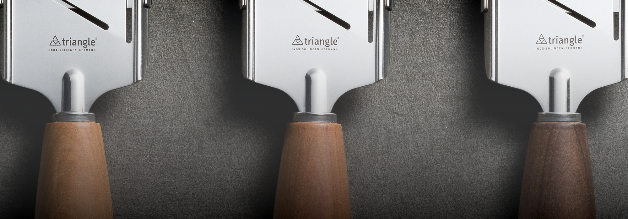 Drei Dreieck-Käsehobel mit Holzgriffen auf dunklem Untergrund