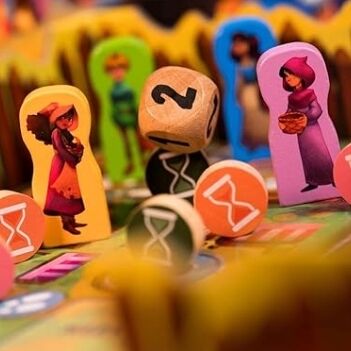Mehrere bunte Spielfiguren, runde und würfelförmige Spielsteine sowie ein Spielbrett des Brettspiels 'Monsterhunger!' sind aus der Nähe zu sehen. Die Szene zeigt detailreich illustrierte Charaktere und abwechslungsreich gestaltete Spielkomponenten. Das Bild vermittelt Freude und gemeinsame Spielerlebnisse für Kinder und Familien.