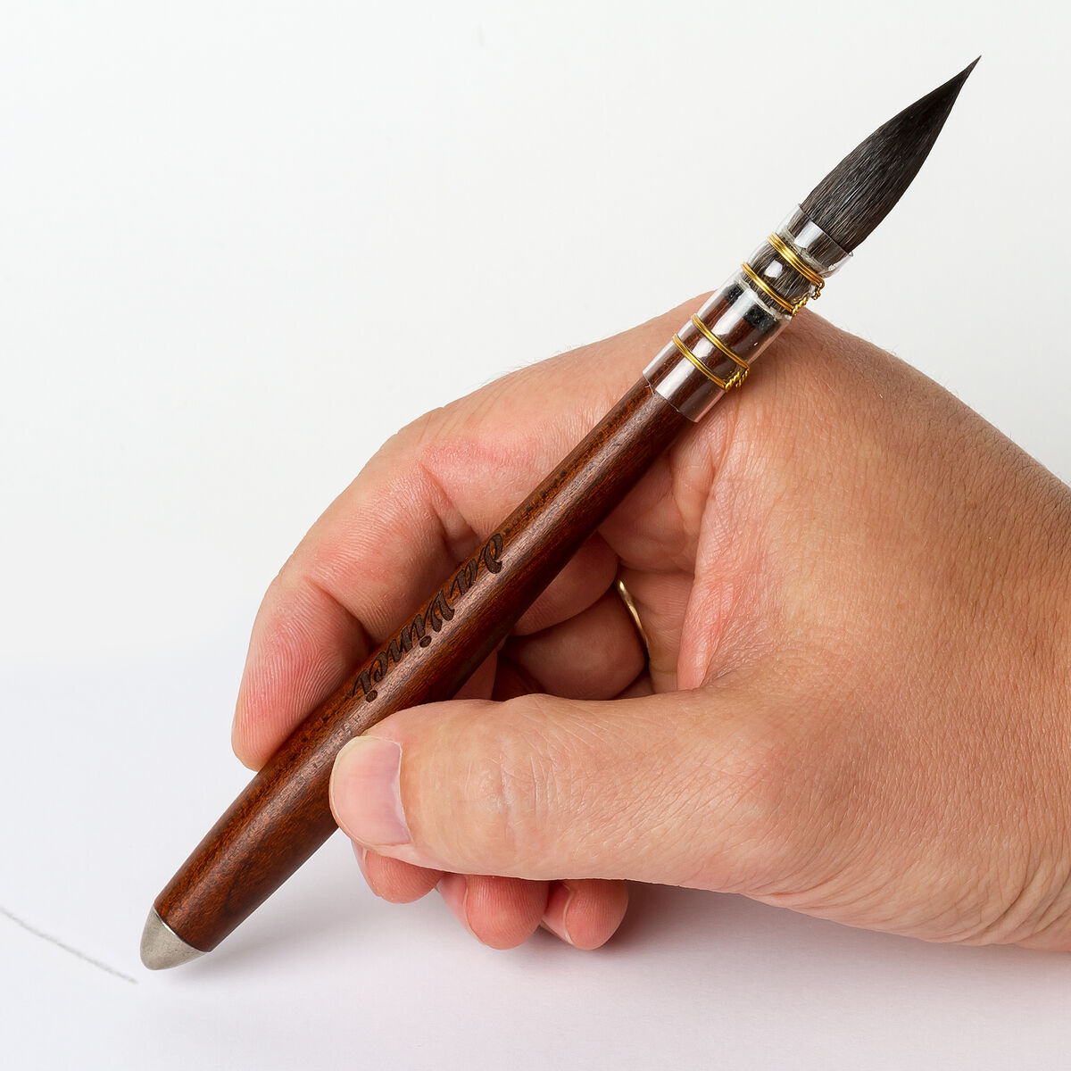 Ein traditioneller Aquarellpinsel mit Ethergraf®-Metallspitze wird von einer Hand gehalten. Der Pinsel hat einen dunkelbraunen Holzgriff und eine feine Spitze.