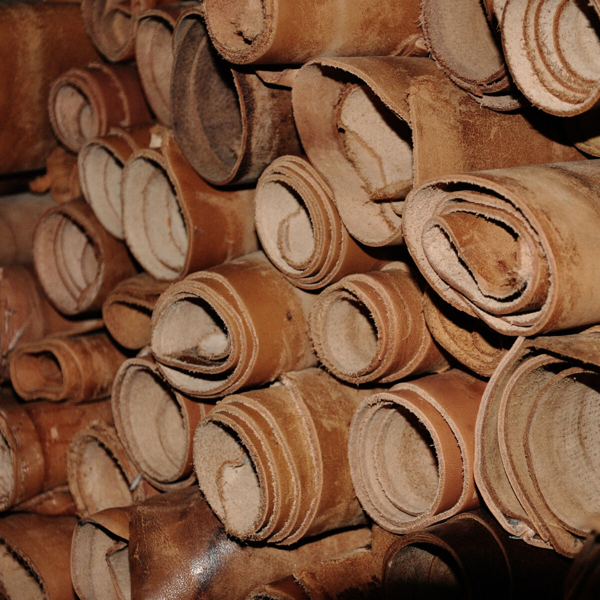 Mehrere aufgerollte Stücke braunes Leder, die eng nebeneinander gestapelt sind. Das Leder hat verschiedene braune und beigetöne und eine leicht raue Oberfläche.