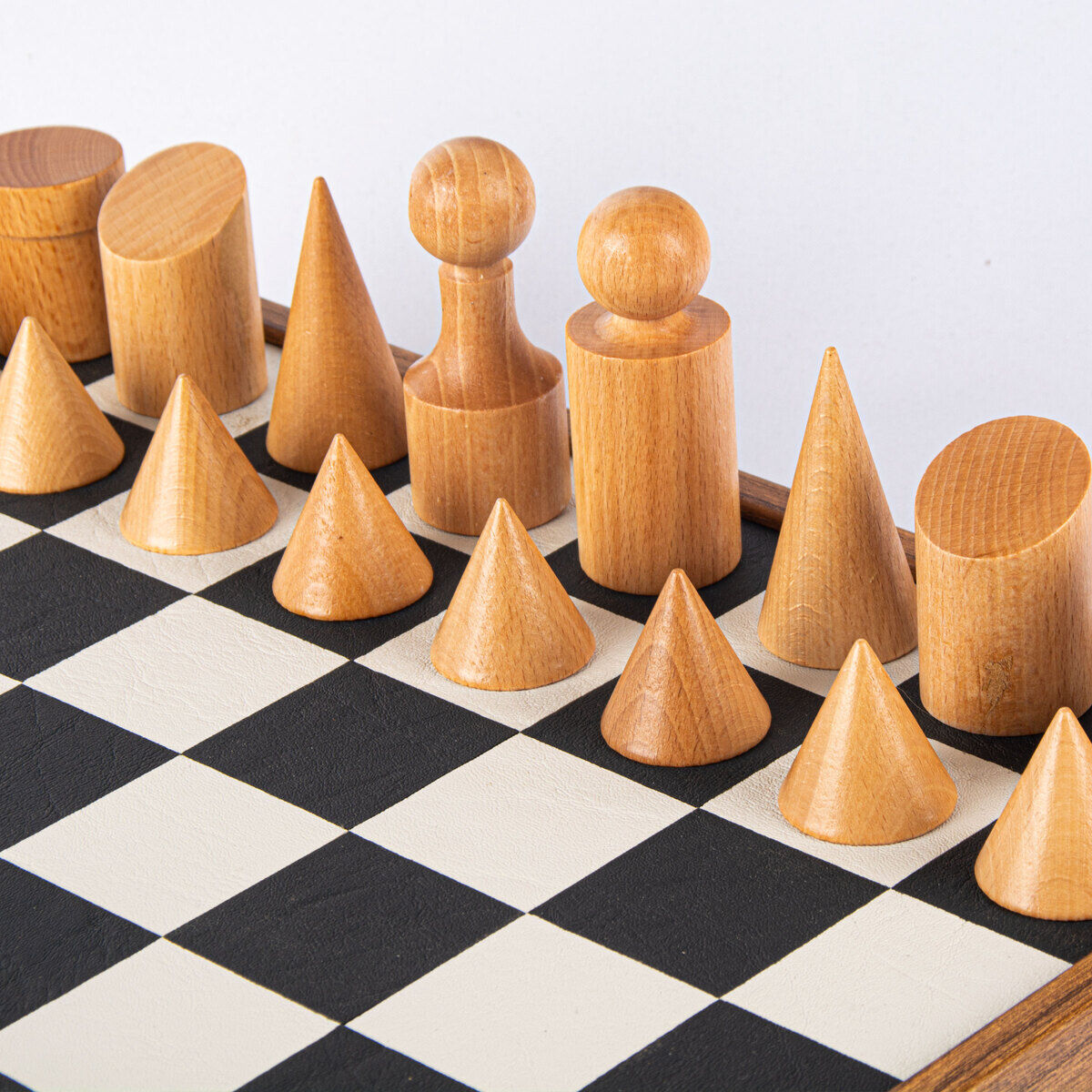 Ein Schachspiel im Bauhaus-Stil mit geometrisch geformten Schachfiguren aus Holz auf einem schwarz-weißen Schachbrett.