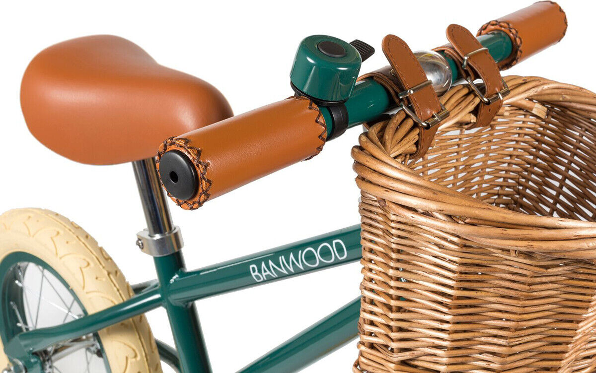 Retro-Laufrad in Grün mit braunem Sattel und Griffen sowie einem geflochtenen Holzkörbchen vorne am Lenker befestigt. Elegantes und umweltfreundliches Design für Kinder.