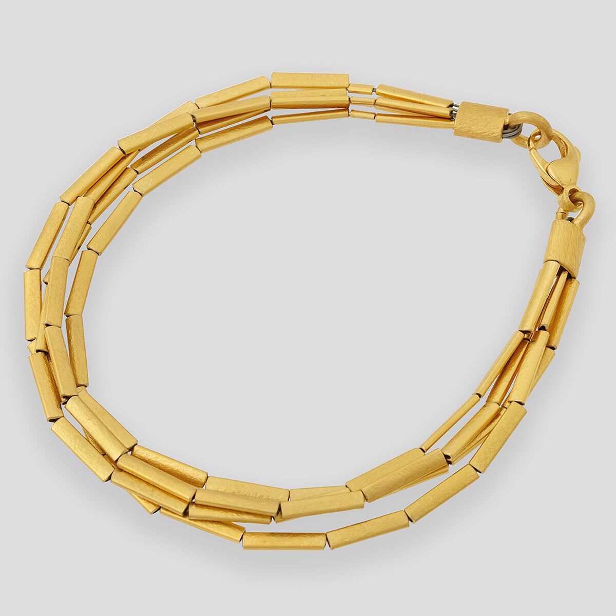 Abgebildet ist ein elegantes Armband aus silbernem Material mit Feingoldplattierung. Das Schmuckstück besteht aus mehreren, dünnen Röhrchen, die gemeinsam ein stilvolles, doppelt gelegtes Design bilden. Es liegt auf neutralgrauem Hintergrund und ist geöffnet abgebildet.