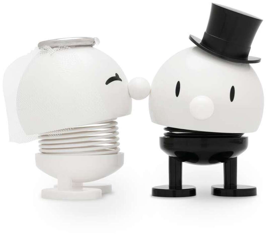 Zwei Figuren im Hoptimist-Design als Braut und Bräutigam: Die Braut ist weiß mit Schleier, der Bräutigam trägt Zylinder und schwarze Beine. Beide blicken sich an, minimalistischer Stil, glatte Oberflächen, freundlicher Ausdruck. Auf weißem Hintergrund.