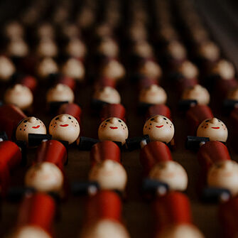 Nahaufnahme einer Reihe von Holzfiguren mit lächelnden Gesichtern, die rote Uniformen tragen und in einem gitterartigen Muster angeordnet sind.