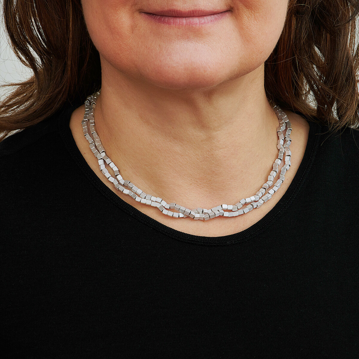 Frau trägt eine silberne Würfelform-Halskette auf einem schwarzen Oberteil.