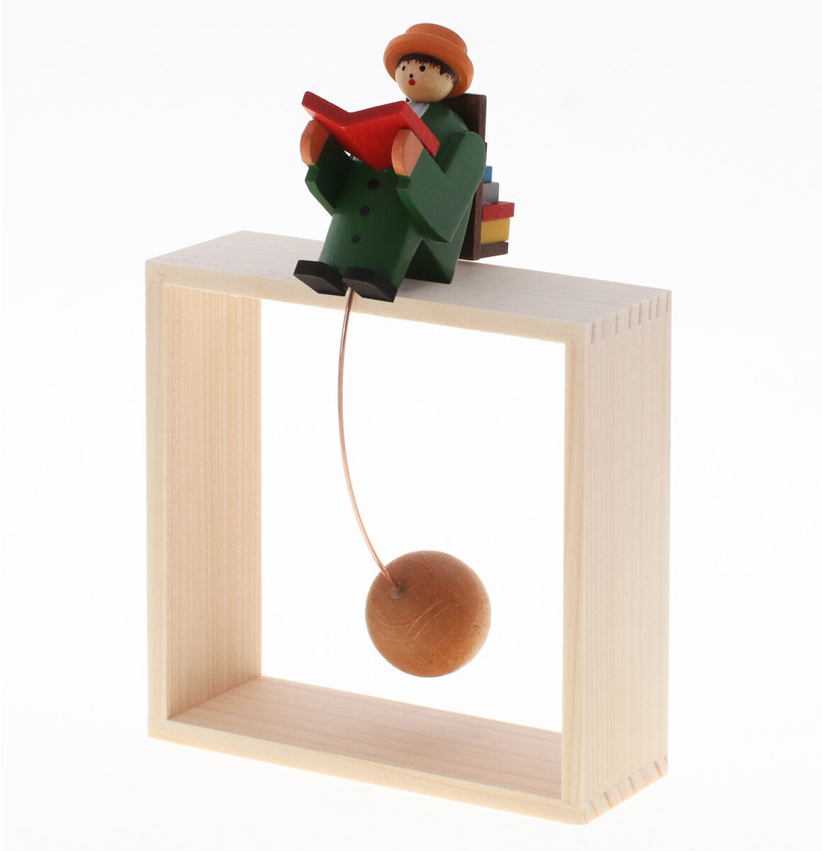 Eine handgefertigte Holzfigur, die einen sitzenden Leser darstellt, auf einer Kante schaukelnd und ein Buch haltend. Die Figur trägt einen grünen Mantel und einen orangefarbenen Hut, mit einem roten Buch in den Händen. Ein rundes Holzelement hängt unter der Figur.