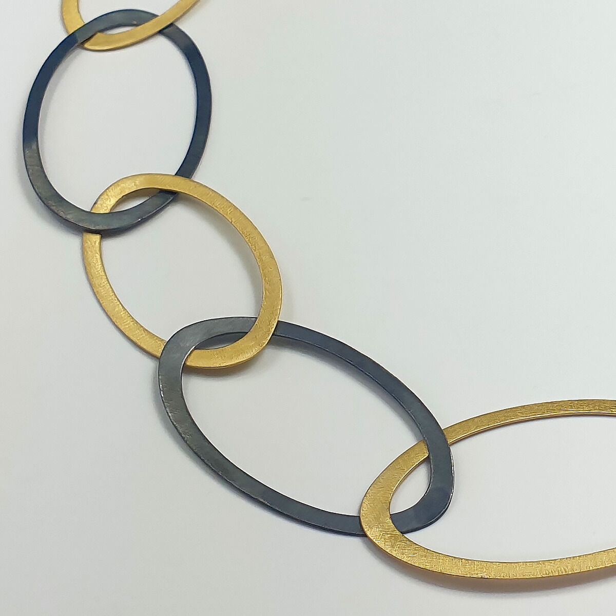 Detailaufnahme des Colliers „Silberringe“ von Maria Rzewuska, bestehend aus abwechselnd goldfarbenen und schwarz oxidierten, ovalen 925er-Silberringen. Die edle Verarbeitung und das elegante, moderne Design verleihen dem Schmuckstück eine zeitlose Ausstrahlung.