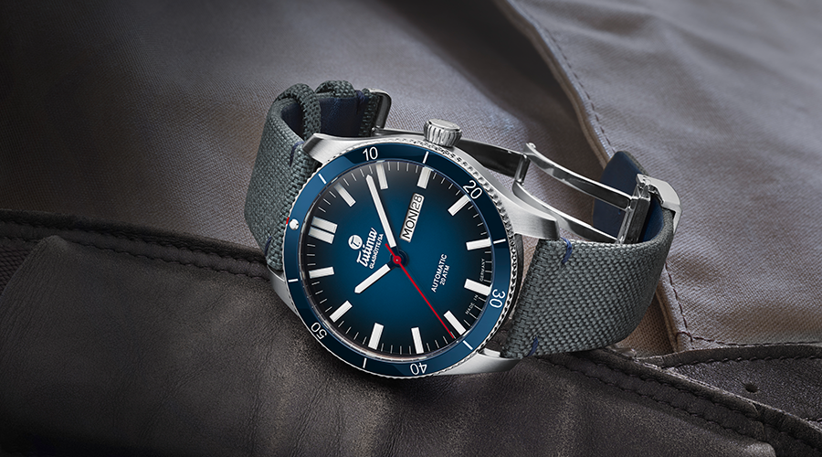 Tutima Herrenuhr mit blauem Zifferblatt, Edelstahlgehäuse und grauem Textilarmband, zeigt Datum und Wochentag