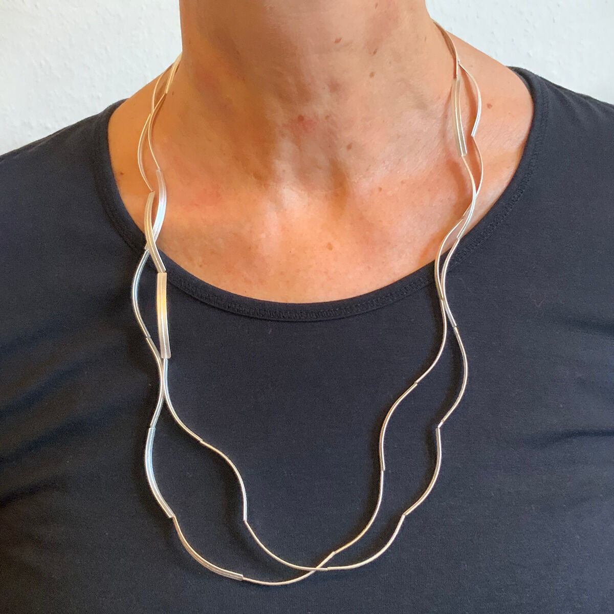 Eine elegante Halskette aus Silber mit einem wellenförmigen Design, getragen von einer Person in einem schwarzen Oberteil.