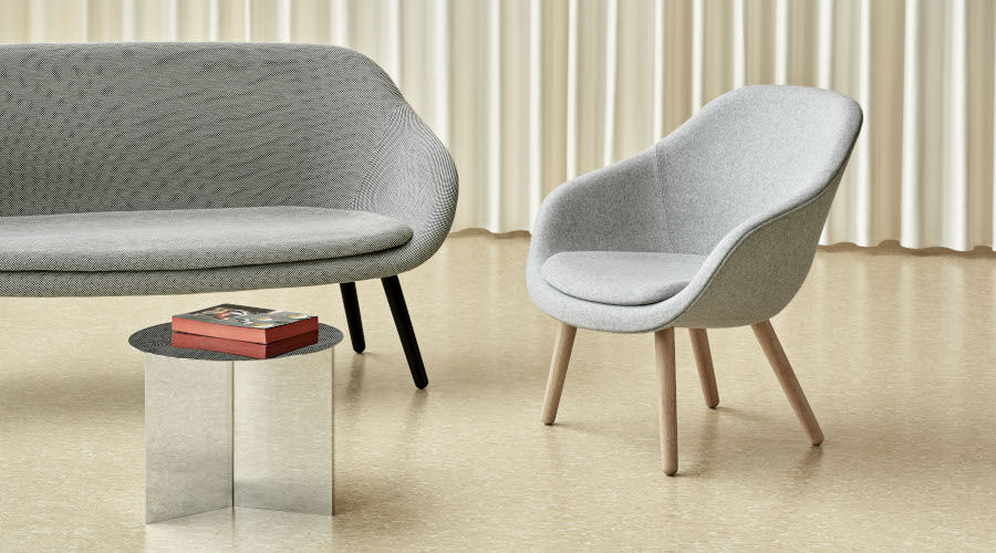 Graues Sofa und grauer Sessel mit Holzbeinen neben einem kleinen runden Beistelltisch mit transparentem Sockel und Buch darauf