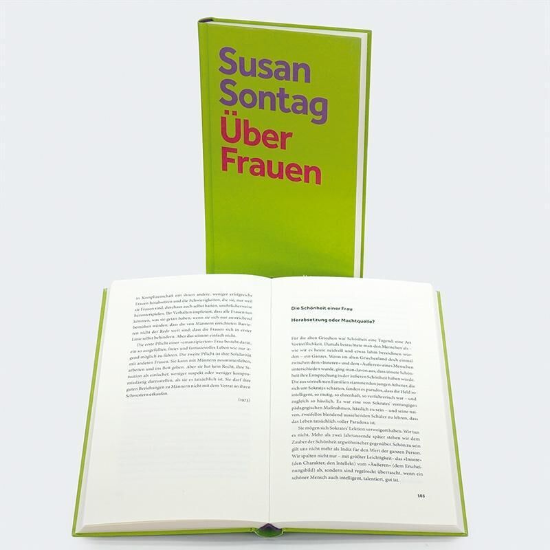 Das Bild zeigt zwei Bücher. Eines steht aufrecht und zeigt den Titel "Susan Sontag: Über Frauen" in großen Buchstaben auf einem grünen Hintergrund. Das andere Buch liegt offen davor und enthüllt Text in hauptsächlich schwarzer Schrift auf weißem Papier.