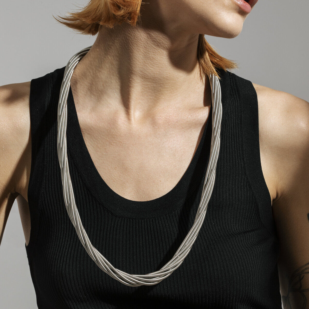 Eine Frau mit kurzen, rötlichen Haaren trägt eine silberne Halskette im Twist-Design und ein schwarzes ärmelloses Oberteil.