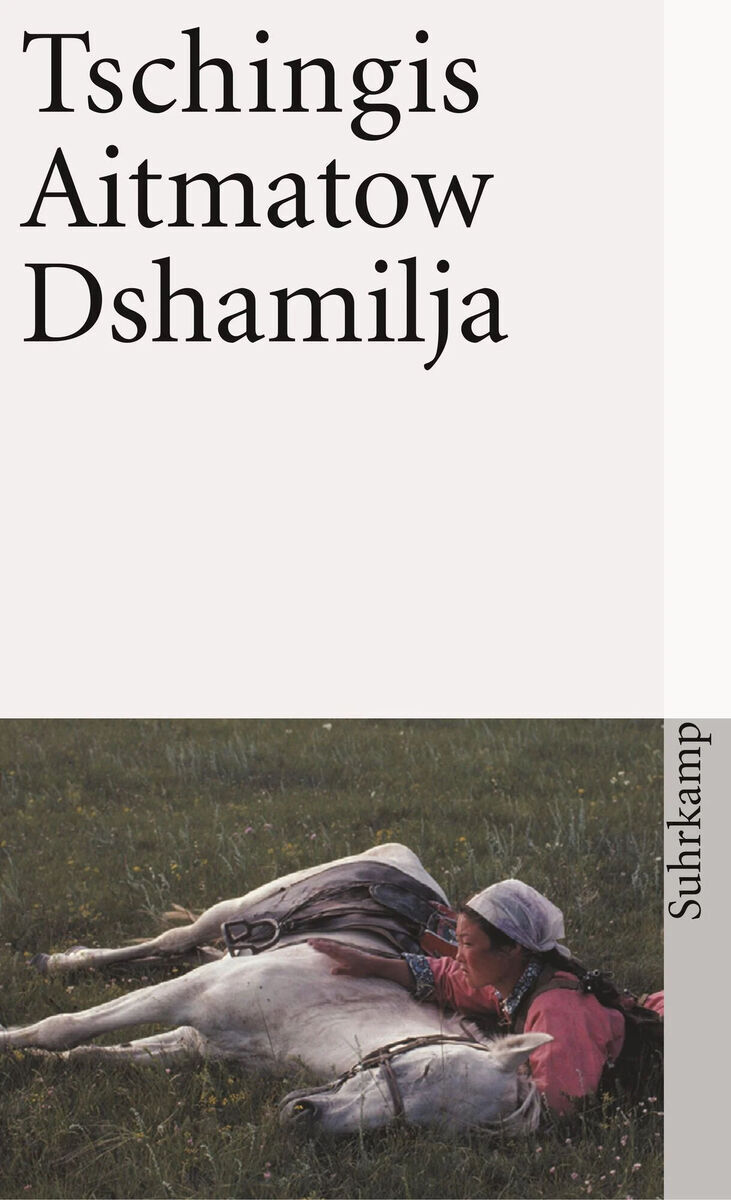 Das Buchcover von 'Tschingis Aitmatow: Dshamilja', veröffentlicht von Suhrkamp Verlag. Es zeigt den Titel in schwarzen Buchstaben auf weißem Hintergrund. Im unteren Drittel ist ein Bild abgebildet, auf dem eine Frau neben einem weißen Pferd auf einer grünen Wiese liegt.