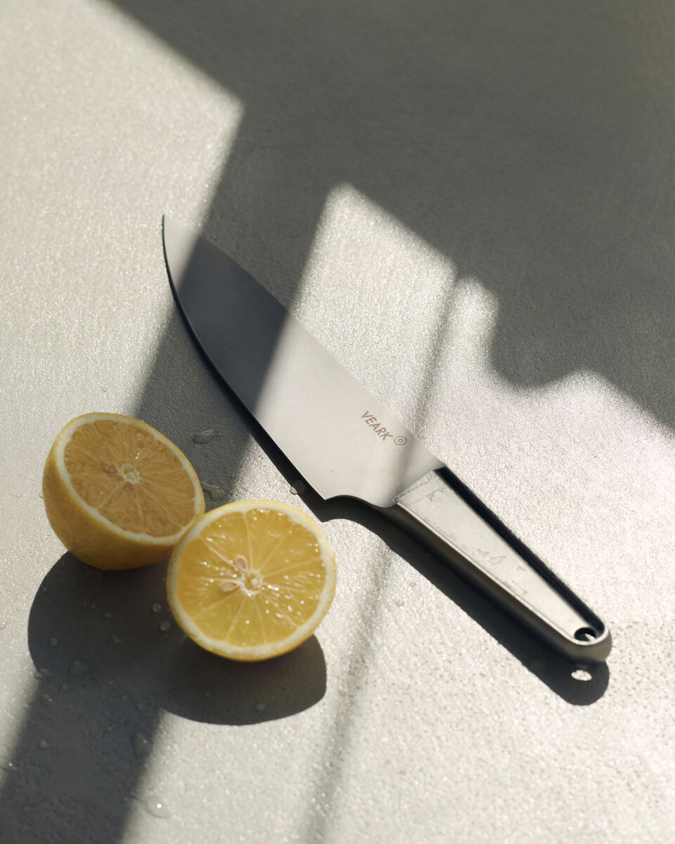 Ein hochwertiges Küchenmesser aus rostfreiem Stahl liegt auf einer grauen Oberfläche neben zwei Hälften einer Zitrone.