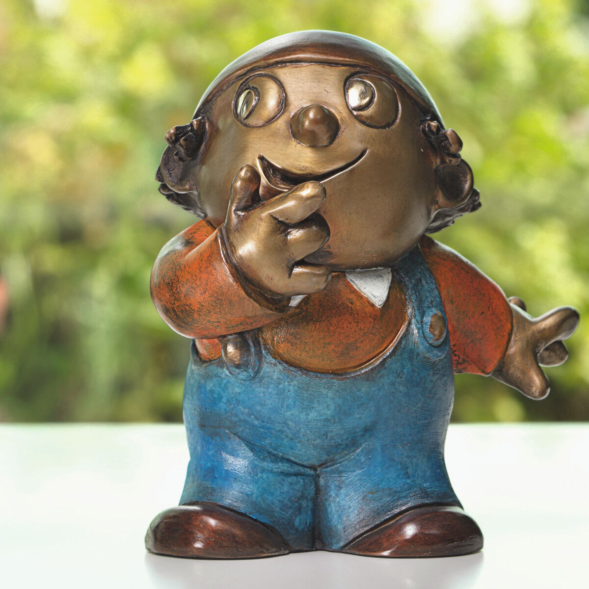 Das Bild zeigt drei detailreiche Bronze-Skulpturen der Mainzelmännchen von Wolf Gerlach. Die Figuren stehen nebeneinander auf einer weißen Oberfläche vor unscharfem, grünem Hintergrund. Jede Figur trägt bunte Kleidung und zeigt eine eigene, verspielte Pose.