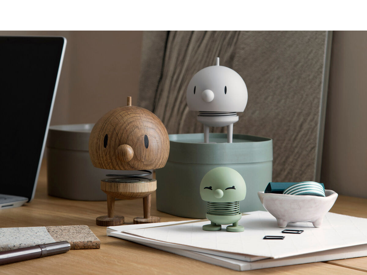 Ein Bild zeigt drei Hoptimist Bumble Figuren in unterschiedlichen Farben (Braun, Weiß, Grün) auf einem Schreibtisch. Im Hintergrund sind Schreibtischartikel und ein Laptop zu sehen.