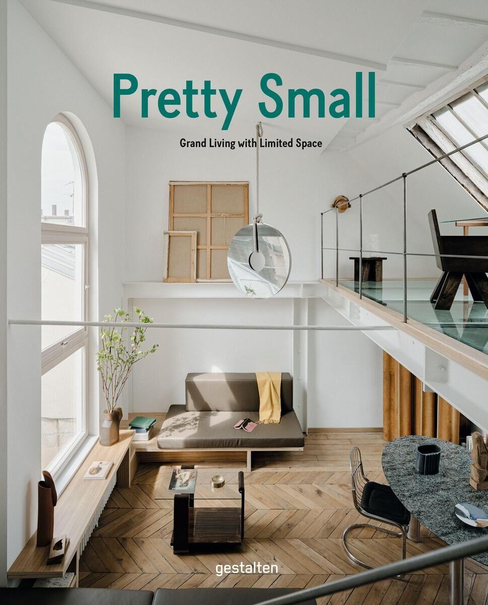 Ein Buch mit dem Titel 'Pretty Small' liegt auf einem hölzernen Boden in einem modern eingerichteten Raum mit weißen Wänden und Glasgeländern. Das Buch behandelt das Thema Wohnen auf kleinem Raum.