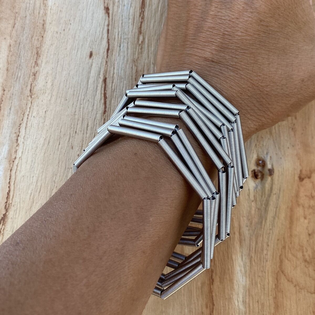 Das Foto zeigt ein silberfarbenes Edelstahlarmband der Marke la molla, Modell "MISTY", am Handgelenk einer Person. Das Armband besteht aus mehreren flexiblen, geometrisch angeordneten Röhrchen und liegt auf einer hell gemaserten Holzoberfläche.