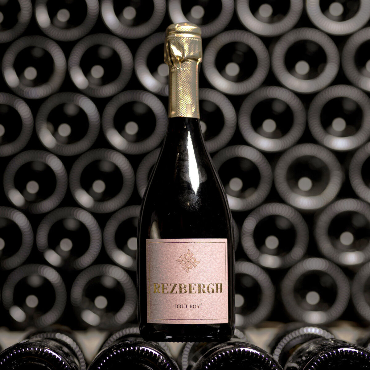Eine edle Flasche Crémant de Luxembourg BRUT ROSÉ steht im Vordergrund eines Regals voller weiterer Flaschen. Das Etikett ist in zartem Rosé gehalten mit goldener Prägung. Die Lichtverhältnisse betonen die Eleganz der Champagnerflasche in stilvollem Ambiente. Perfekt geeignet für festliche Anlässe und Weinliebhaber.