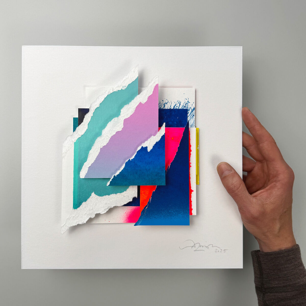 Originalkunstwerk „Unikat »Colors in Space - No.53«“ von Daniel Lisson in weißem Lindenholzrahmen. Geschichtete, gerissene und geschnittene Collageelemente aus Siebdruck und Sprühlack. Farbige Flächen in Türkis, Rosa, Blau, Magenta, teils mit weißer Textur, signiert und datiert.