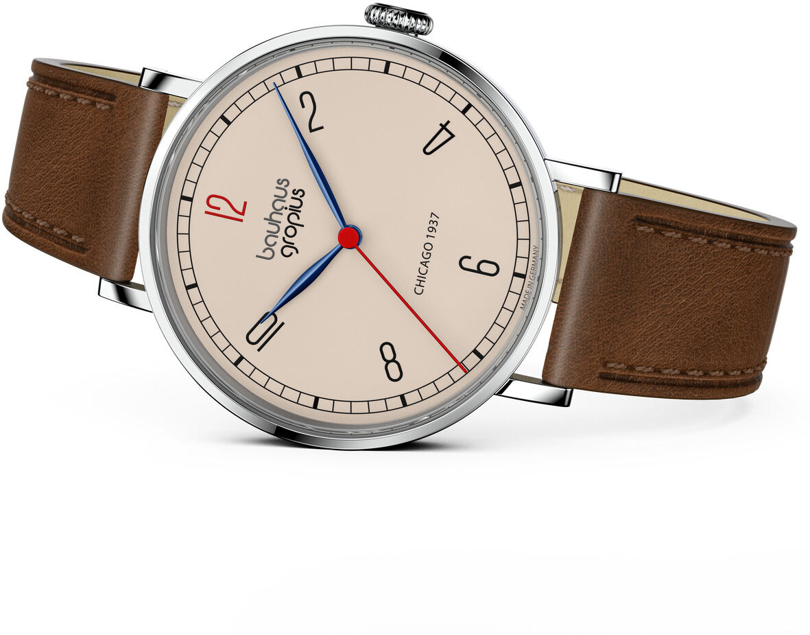 Zeitlos elegante Armbanduhr der ZEIT-Sonderedition mit Bauhaus-inspiriertem Design von Walter Gropius. Die Uhr hat ein rundes silbernes Gehäuse, ein beiges Zifferblatt mit minimalistischen schwarzen Indizes, eine rote Zwölf und einen kontrastreichen blauen Sekundenzeiger. Das braune Lederarmband rundet das klassische Erscheinungsbild ab.