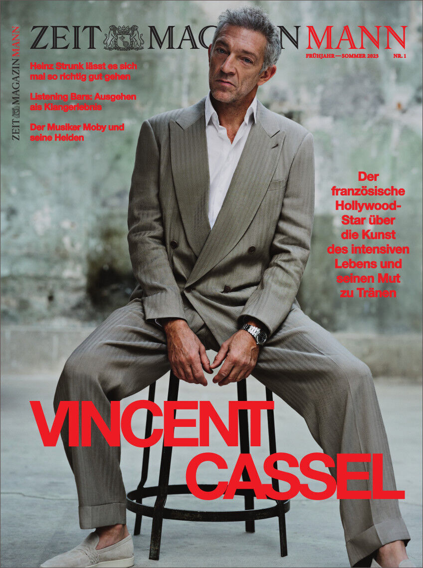 Cover des ZEITmagazin MANN 1/23 mit einem Bild von Vincent Cassel in einem beigefarbenen Anzug. Rechts vom Bild befinden sich rote Texte auf Deutsch, die auf Interviews und Artikel im Magazin hinweisen. Der Hintergrund ist grau und strukturiert.