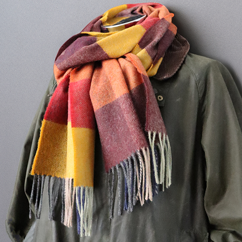 Schal mit großem Karomuster und Fransen, um einen dunkelgrünen Mantel gelegt.