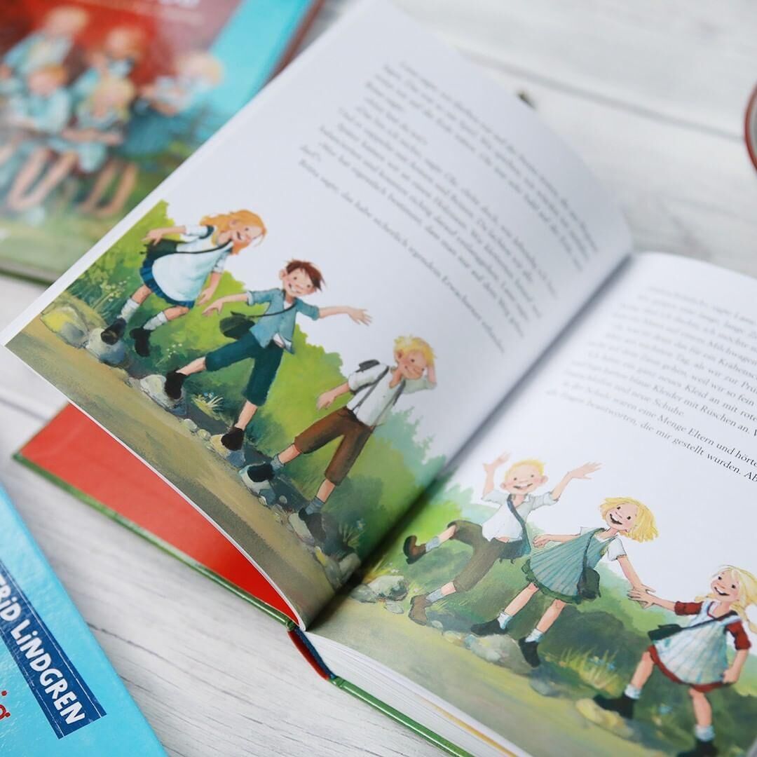 Das Bild zeigt das aufgeschlagene Buch 'Wir Kinder aus Bullerbü' von Astrid Lindgren, illustriert mit Szenen von spielenden Kindern.