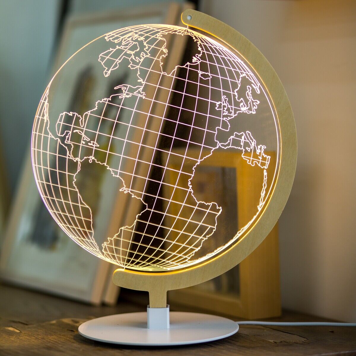 Die LED-Leuchte GLOBE zeigt eine stilisierte Weltkarte in warmem Gelb- und Weißlicht. Sie steht auf einem Holztisch, umgeben von gerahmten Bildern. Ideal für moderne Wohnzimmer- und Kinderzimmerdekoration.