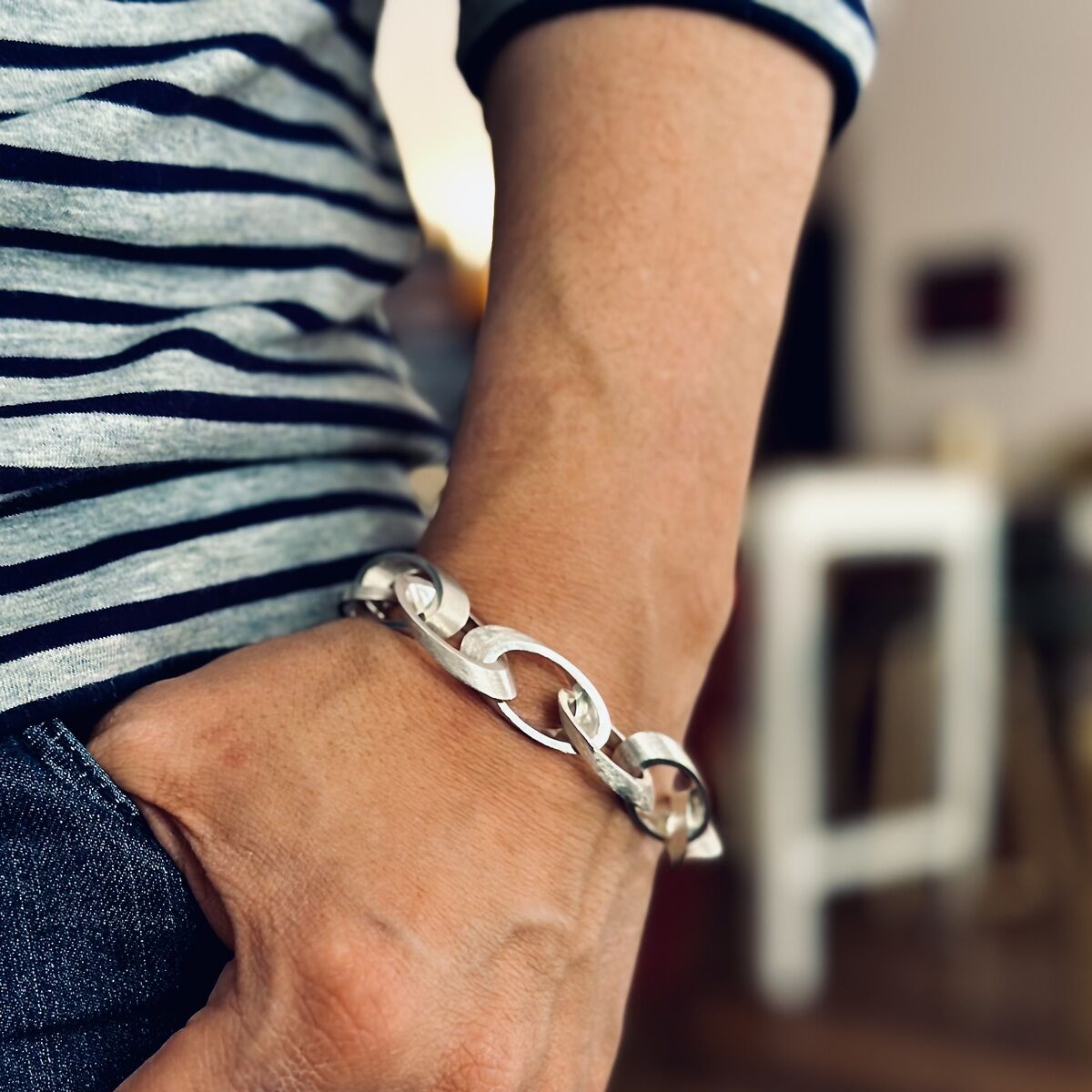 Ein silbernes Armband mit ovalen Gliedern, getragen von einer Person in gestreiftem Oberteil und Jeans, zeigt einen eleganten und modernen Stil.