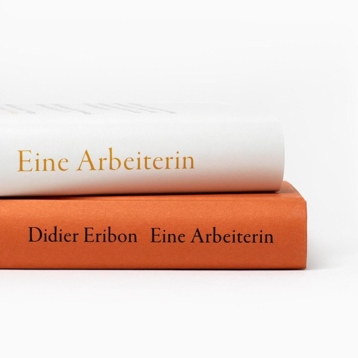 Zwei Bücher übereinander gestapelt: das obere Buch hat einen weißen Einband mit dem Titel 'Eine Arbeiterin', das untere Buch hat einen orangefarbenen Einband mit dem Text Didier Eribon Eine Arbeiterin.